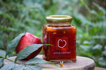 Jar of apple chutney with a red label on a wooden surface with greenery in the background